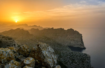 Rock formation in sea against sky during sunset