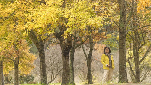 Rear view of woman standing amidst trees during autumn