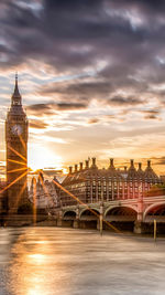 View of bridge over thames river in city against cloudy sky during sunset