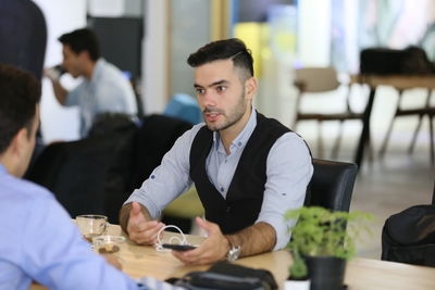 Smiling businessman and colleague talking while sitting on table