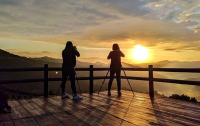 Silhouette women standing by railing against sky during sunset