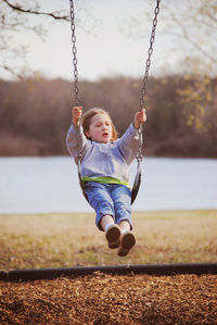 Girl swinging at lakeshore against sky