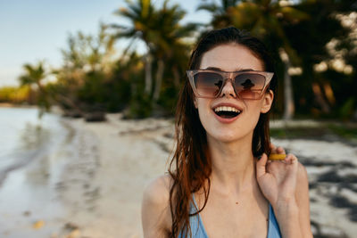 Portrait of young woman wearing sunglasses while standing on beach