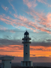 Lighthouse by sea against sky during sunset