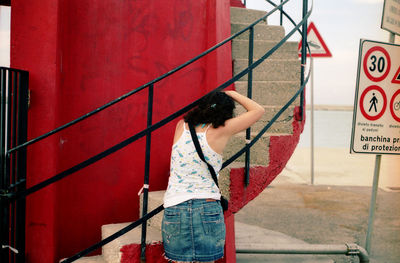 Woman standing by railing against red wall
