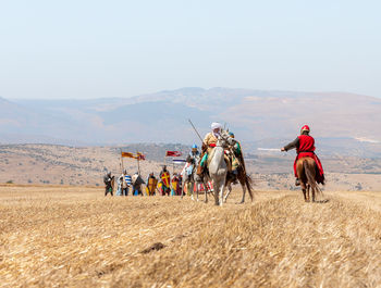 People riding horses on field against sky