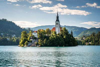 Scenic view of building by trees in lake by mountains against sky