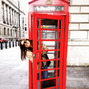 Happy young woman at door of telephone booth