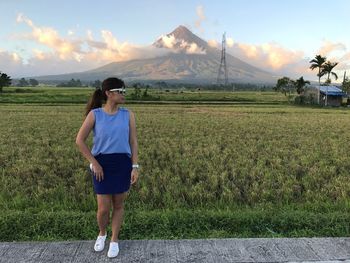 Young woman standing by grassy field against mountain