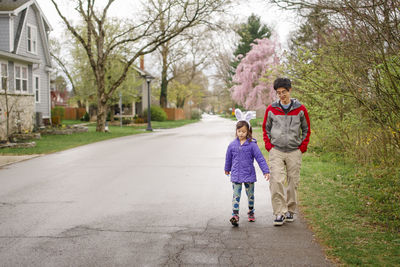 A child wearing bunny ears walks with her father on street in spring