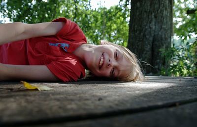 Portrait of smiling boy lying on footpath against trees