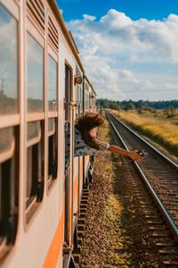 Rear view of happy woman holding mobile phone peeking through window while traveling in train