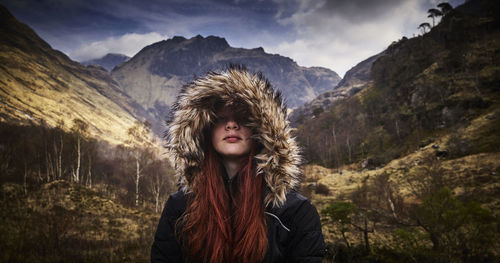 Smiling young woman wearing hooded jacket against snow covered mountains