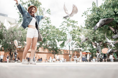 Full length of happy woman with arms raised against trees