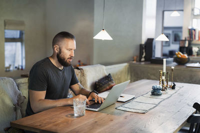 Man working on laptop at dining table in house