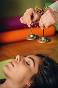 Cropped hands of therapist holding bells by young woman at spa