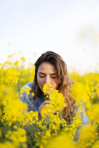 Portrait of young woman smelling yellow flower in field