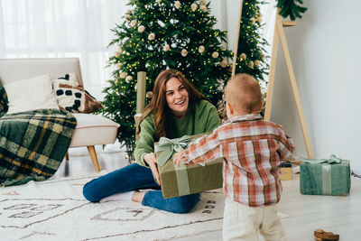 Young happy kind redhead diverse woman holds out a gift box to a child. 