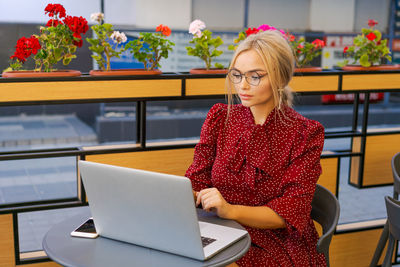 Beautiful woman works on laptop in coffee shop and using mobile phone in a red