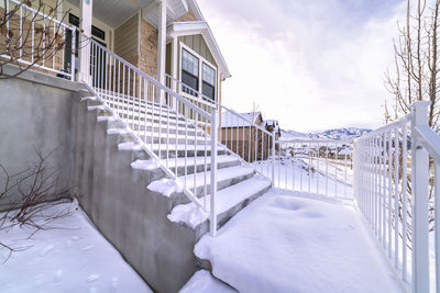 Snow covered fence by building against sky