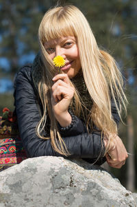 Portrait of woman holding yellow flower on rock