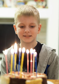 Cute boy looking at lit candles on birthday cake at home