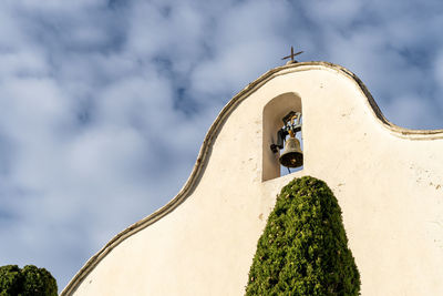 Exterior, bell on the facade of a hermitage, with a cloudy blue sky.