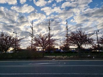 Road by trees against sky at sunset