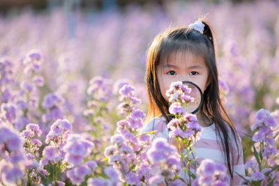 Close-up portrait of girl holding magnifying glass by purple flowering plants