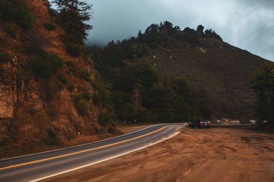 Road amidst trees and mountains against sky