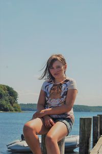 Portrait of girl sitting at lakeshore against sky