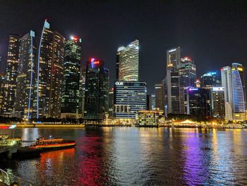 Illuminated city by river against sky at night