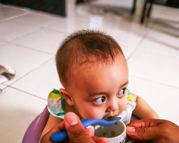 Cropped hands of person feeding baby girl at home