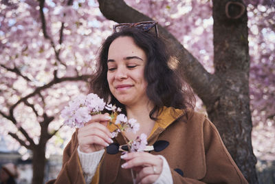 Young woman standing under cherry blossom and holding branch