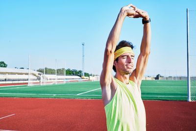 Portrait of smiling man with arms raised against sky