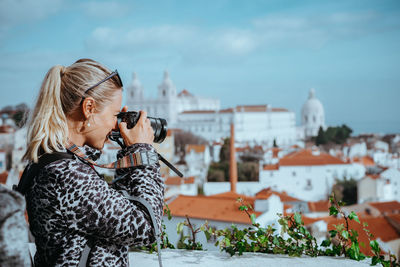 Young woman photographing with cityscape against sky