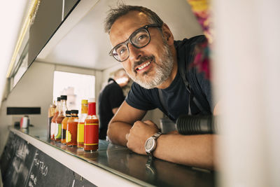 Portrait of happy male chef leaning on counter at food truck
