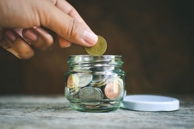 Cropped hand putting coin in glass container on wooden table