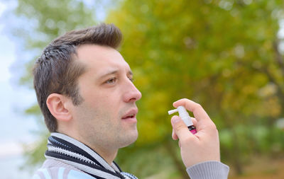 Close-up of man holding inhaler against trees