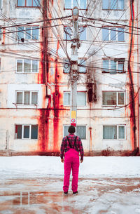 Rear view of man standing against abandoned building during winter