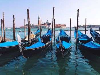 Gondolas moored by wooden posts in grand canal against sky