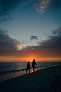 Silhouette people on beach against sky during sunset