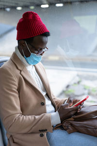 Young man wearing mask using smart phone sitting in bus