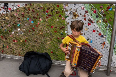 High angle view of boy playing accordion by love locks on bridge railing