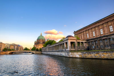 View of buildings by river against sky in city