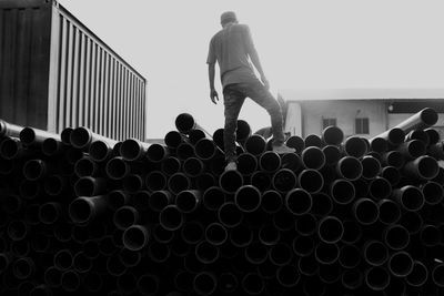 Man standing on stack of pipes against sky