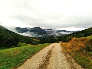 Dirt road amidst green landscape against sky