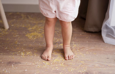 Toddler girl legs standing on messy floor after playing with grain, nuts, pasta and rice