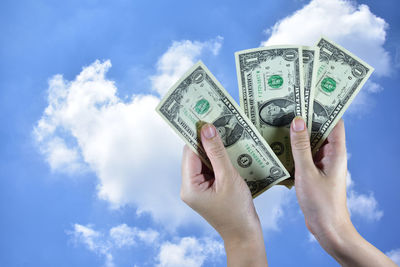 Close-up of person holding currency against blue sky