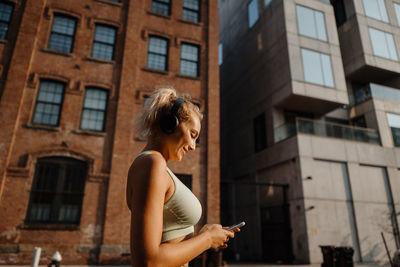 Side view of young woman standing against building